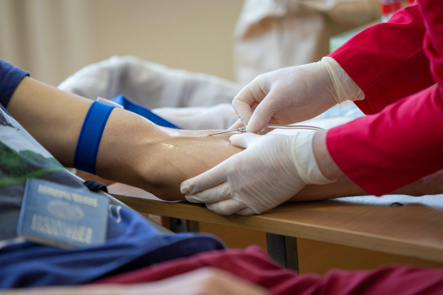 Medical professional drawing blood from donor's arm in a clinical setting.
