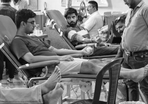 Men donating blood in a healthcare setting, grayscale photography.